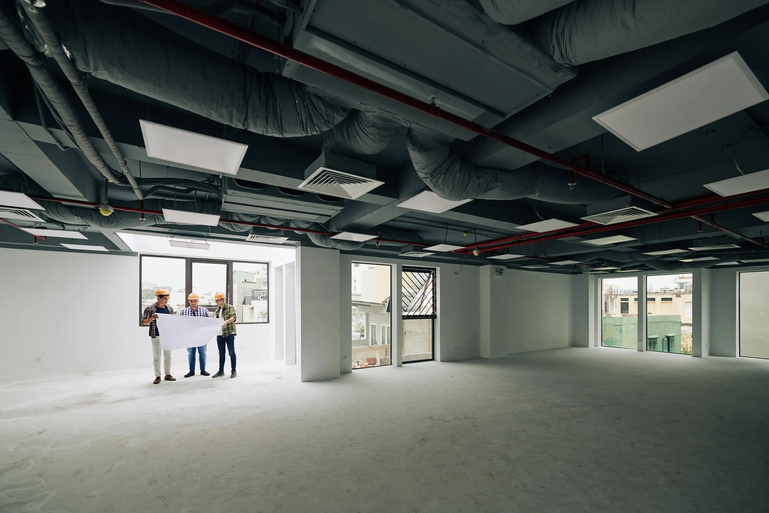 Construction workers examining plans in empty room.